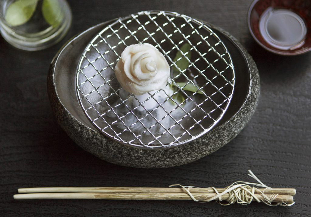 shallow bowl with california black cod sashimi next to a pair of rustic chopsticks